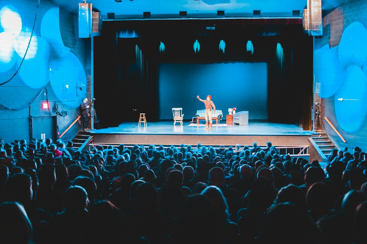 A small, full theatre seen from the audience, with an actress on stage